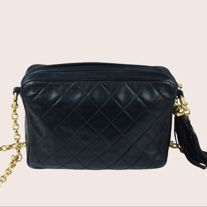 Nandalee black lambskin Chanel Single Flap vintage camera bag with gold chain and tassel detail.