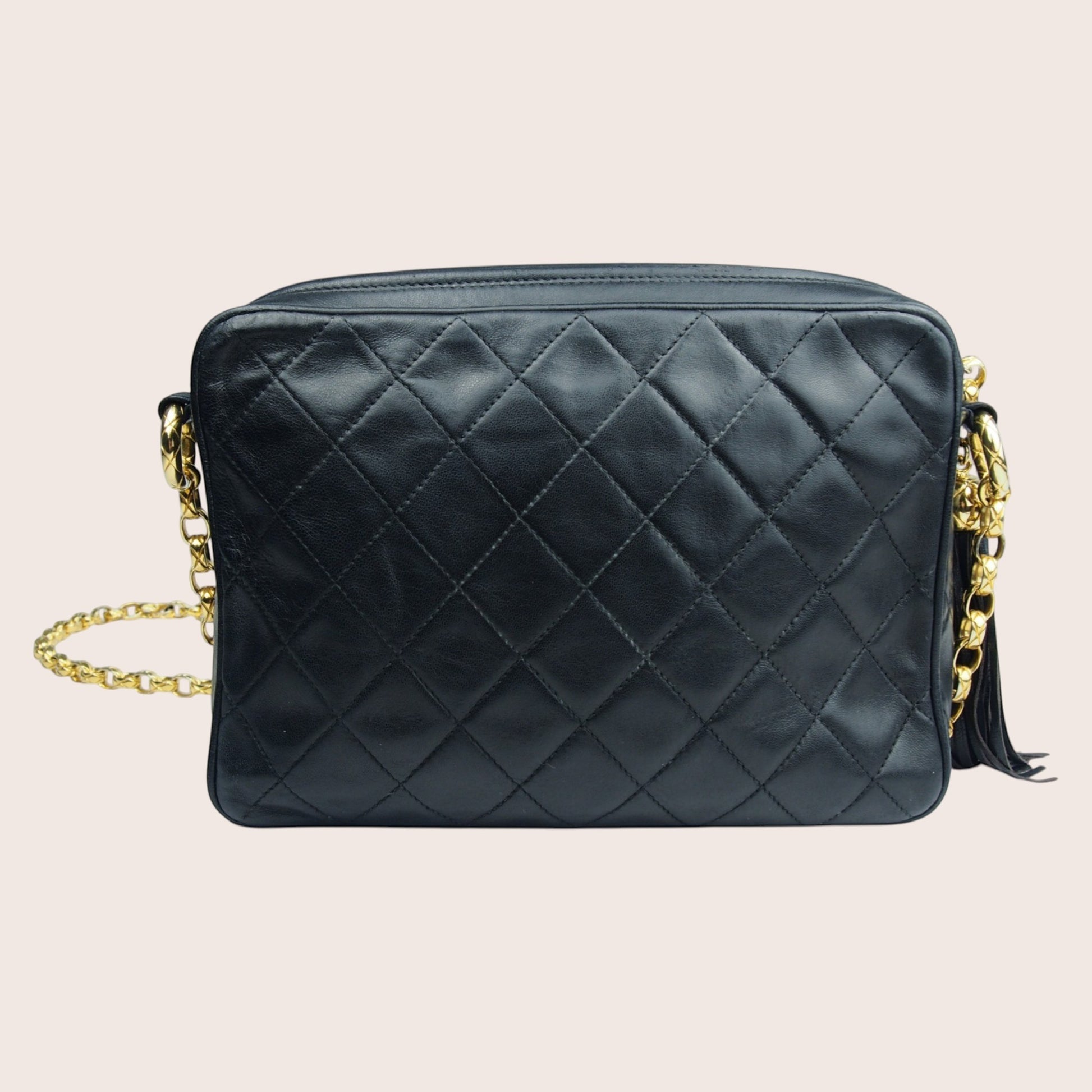 Nandalee black quilted lambskin Chanel camera bag with gold chain strap and tassel detail.